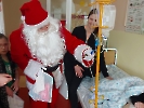 Mikołaj stoi przy łóżku dziecka, w ręku trzyma paczkę z prezentem.