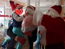 Mikołaj wręcza dziecku prezent. Dziecko jest trzymane na rękach przez rodzica.