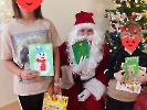 Zdjęcie przy choince, Mikołaj i dwoje dzieci, wszyscy trzymają kartki świąteczne.
