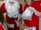 Mikołaj i kobieta w czerwonej sukience, która trzyma paczkę z prezentem.